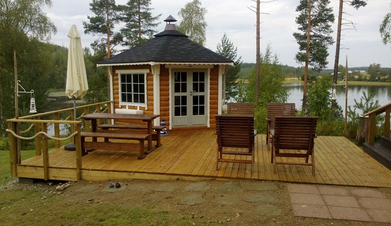 Grillpavillon Victoria 9,2 m² braun mit schwarzen Schindeln auf Veranda vor See