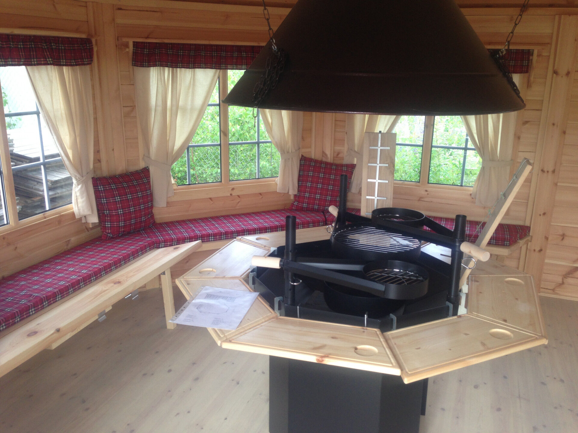 Grillpavillon Victoria Oval 18 m² Innenansicht Schwenkgrill, Rauchabzug, Flammbretter, Einhängetische, rote Sitzkissen