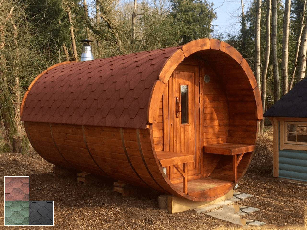 Fass-Sauna Premium aus Thermoholz mit Außenbänken und Holztür mit Glaseinsatz in Ausstellung vor Wald